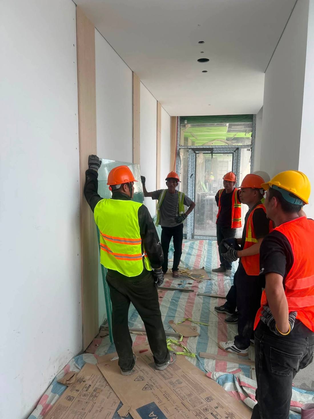Nhóm nhân công áo phản quang cùng nhau di chuyển tấm kính lớn trong công trình