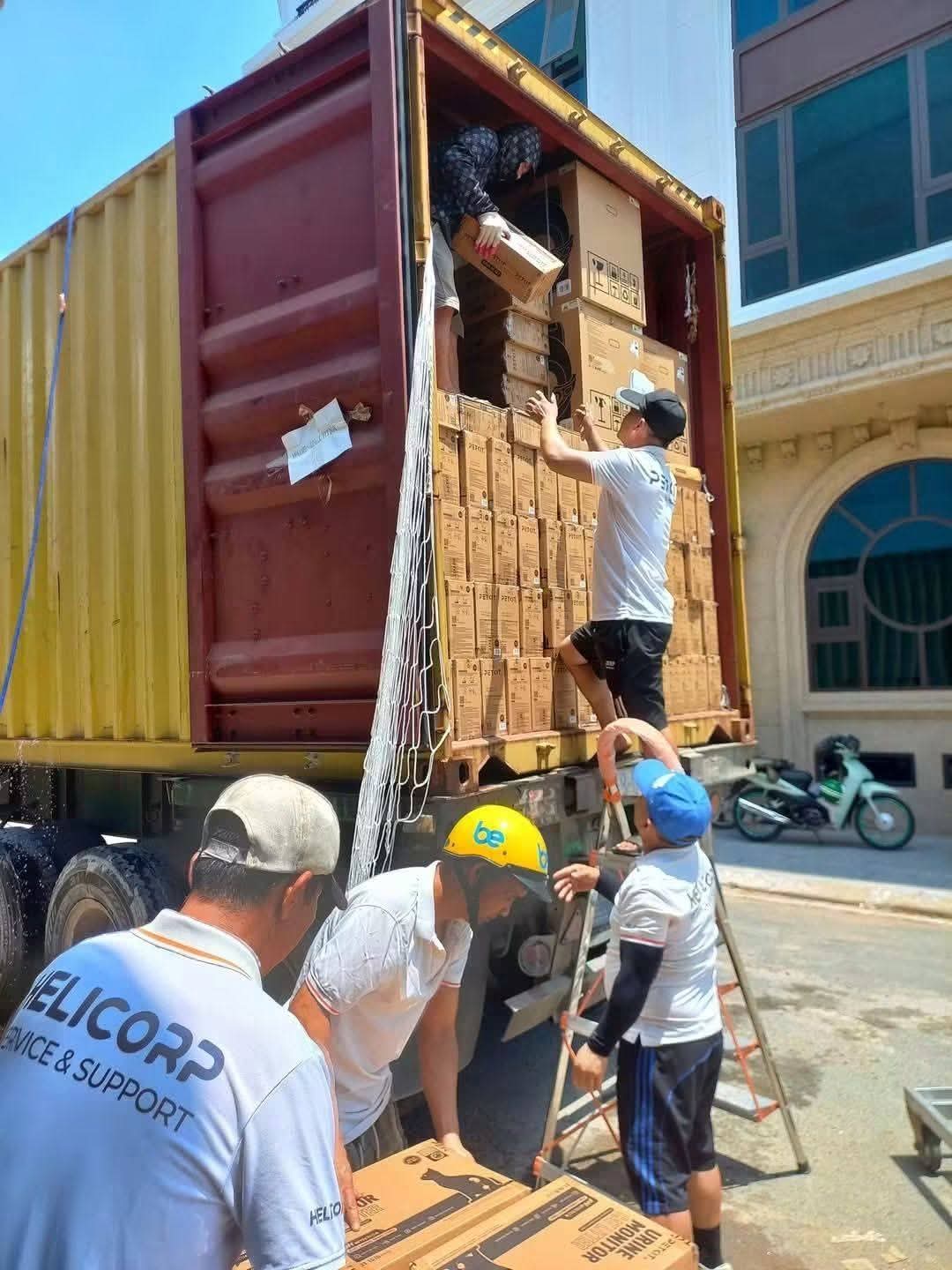 Đội nhân công đồng phục dỡ thùng thiết bị từ container theo dây chuyền