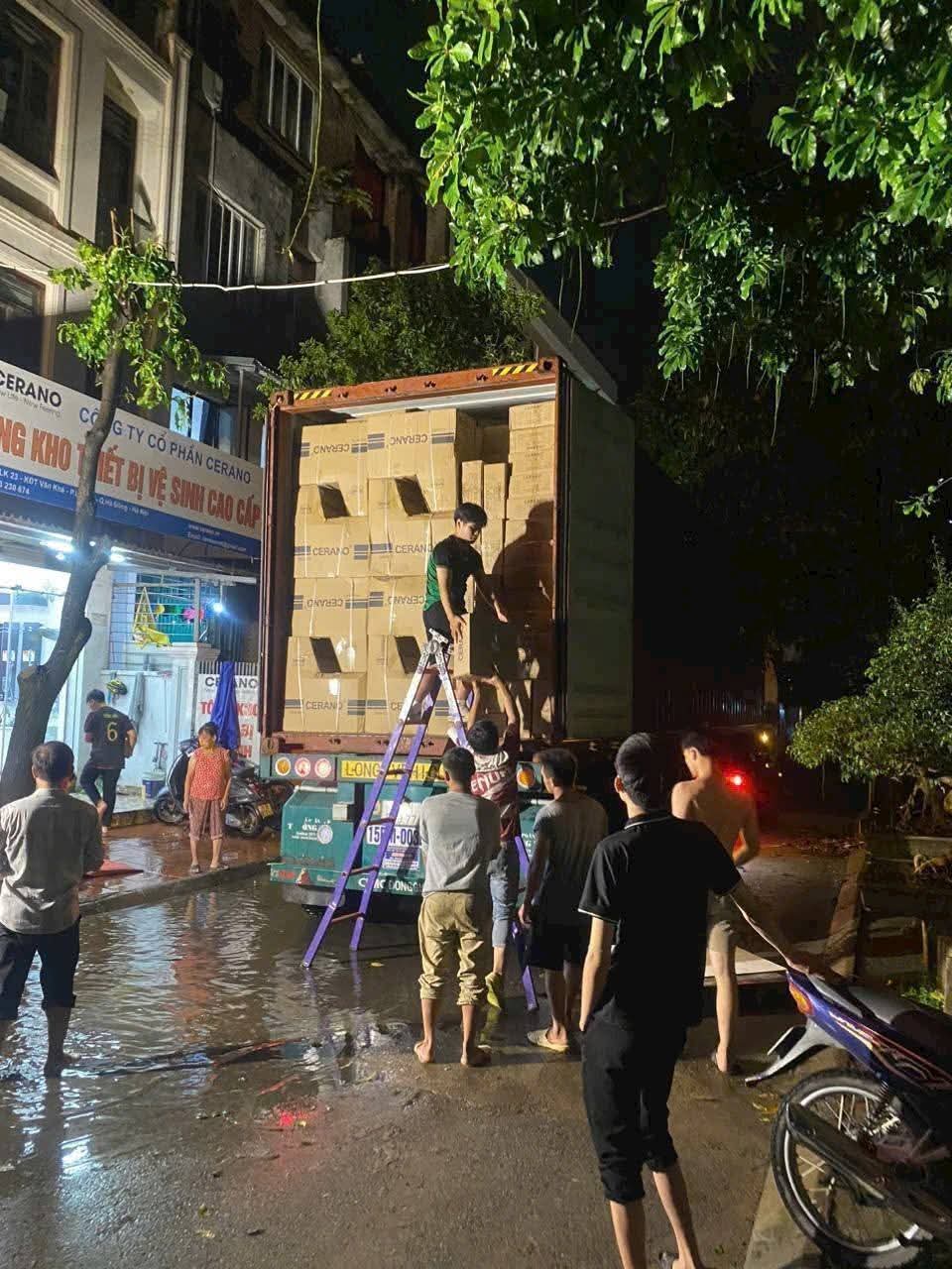Đội nhân công dỡ thùng carton từ container xuống trước nhà vào buổi tối