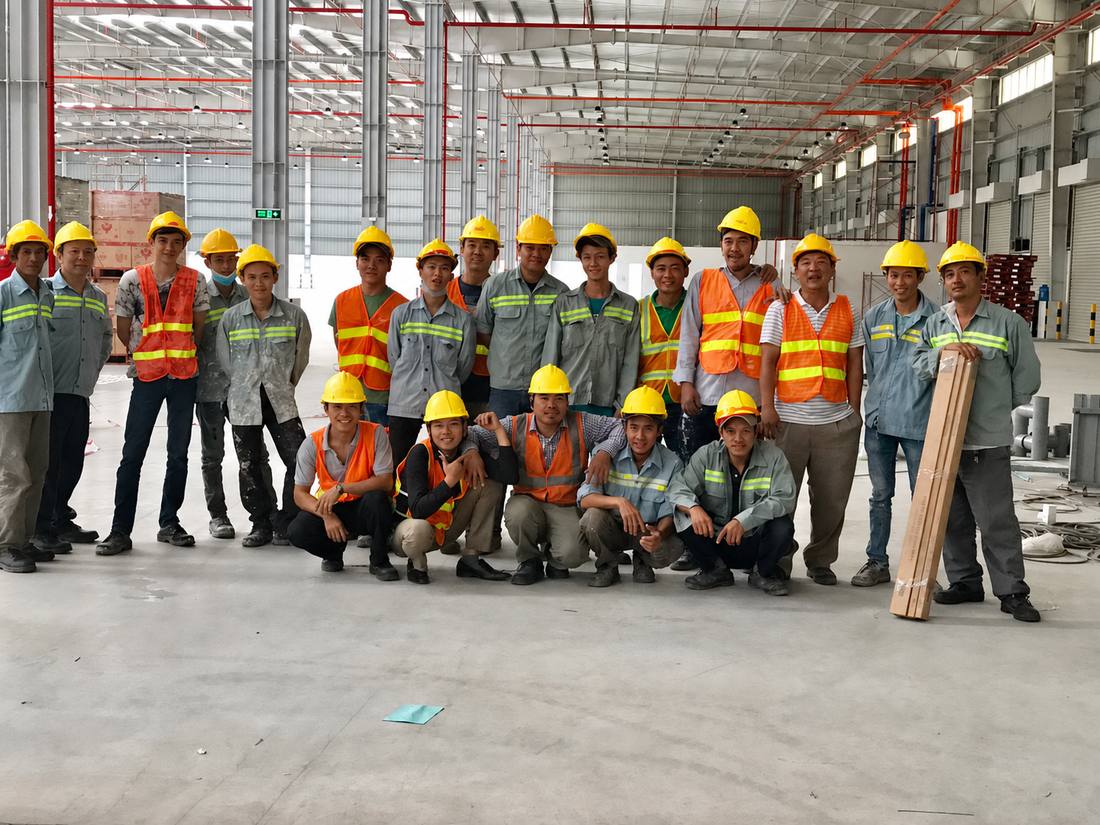 Đội ngũ hơn 20 nhân công Bốc Xếp Sài Gòn đội mũ bảo hộ, mặc áo phản quang trong nhà xưởng